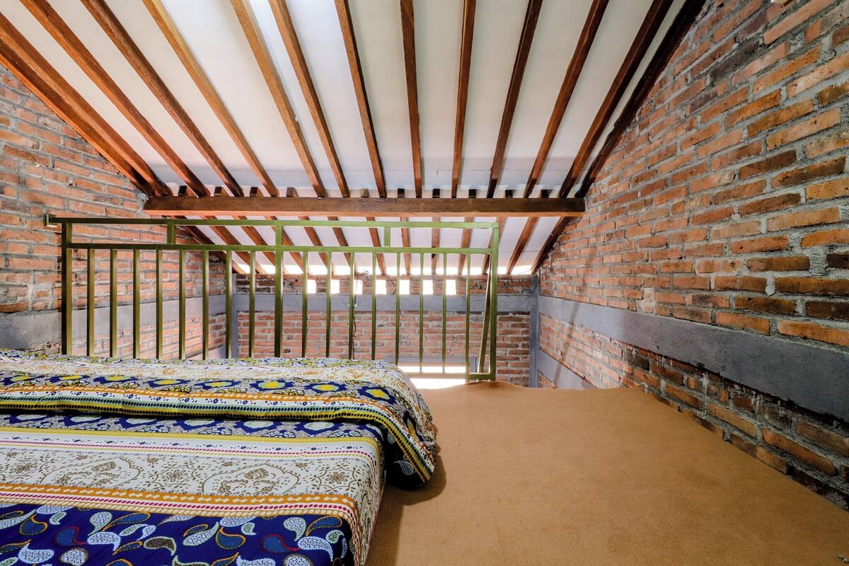 A room with a sloped ceiling, exposed wooden beams, a brick wall, and a bed with patterned bedding.