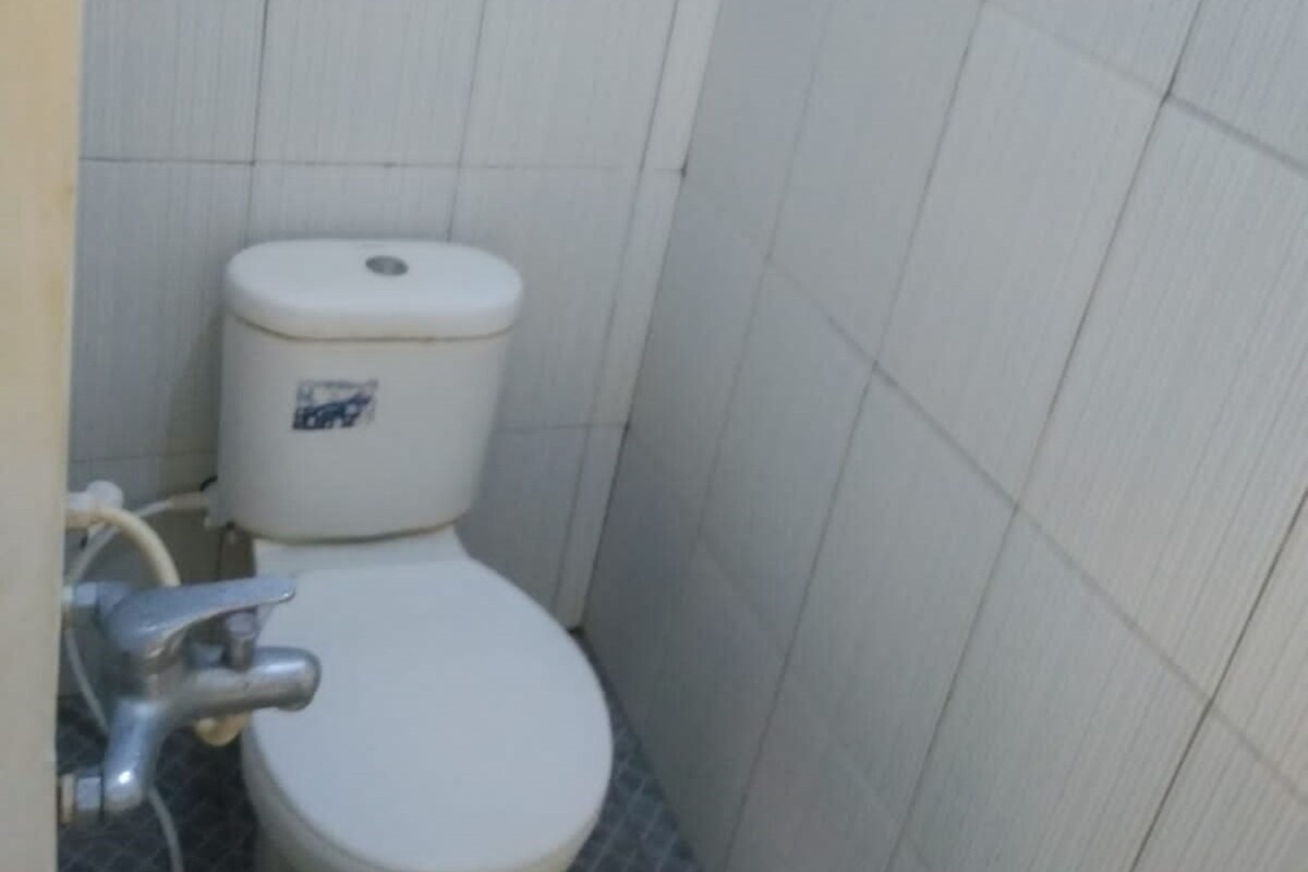 A small, compact bathroom with a white toilet, a visible pipe, and a tiled floor.