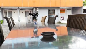 An outdoor dining area with a glass table, wicker chairs, and a potted plant. - Ratu Guesthouse (Depok)