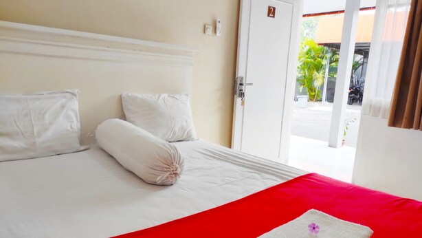 A hotel room with a bed, a red bedspread, and a white pillow. - Ratu Guesthouse (Depok)