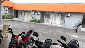 A courtyard with a paved ground, several air conditioning units mounted on the building, and multiple motorcycles parked. - Ratu Guesthouse (Depok)