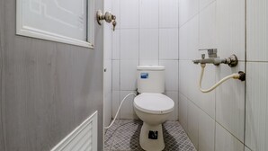 A small, compact bathroom with a toilet, a wall-mounted sink, and a shower area. - Ratu Guesthouse (Depok)