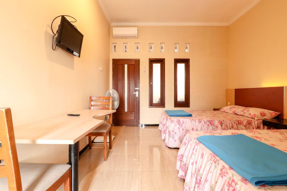 Una habitación de hotel con escritorio, dos camas, una silla y televisión montada en la pared.