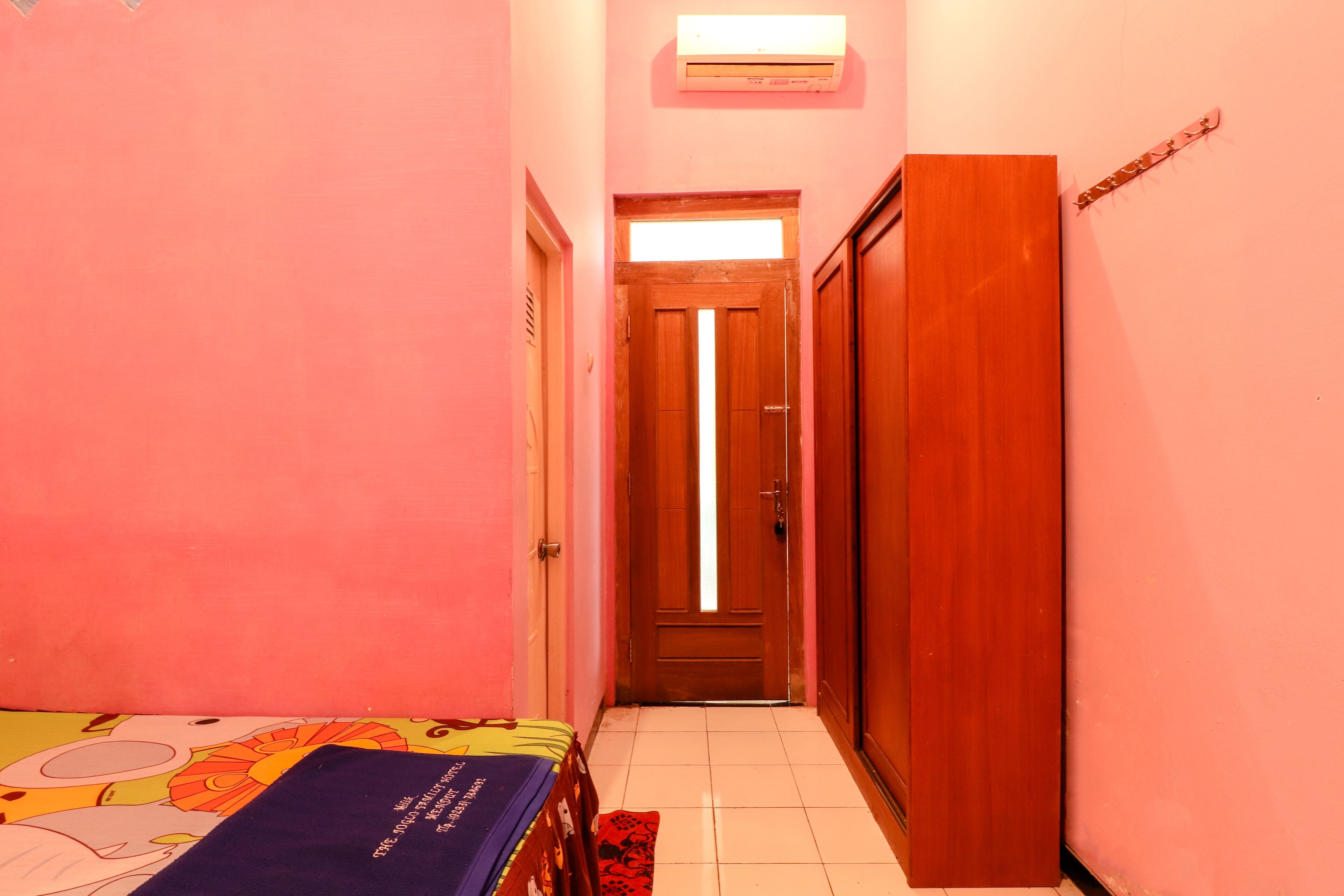 A narrow hallway with a bed on the left, a wooden door at the end, and a wall-mounted air conditioner.