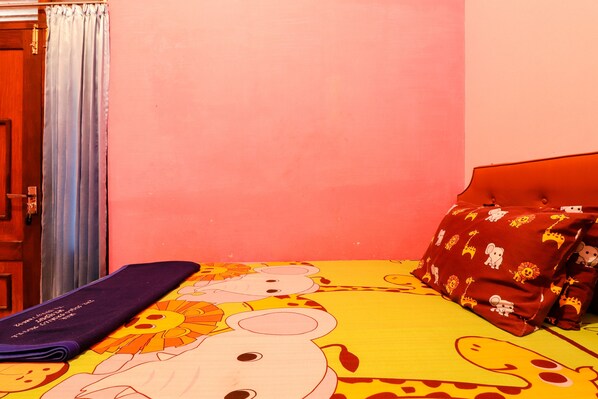 A room with a bed featuring a colorful cartoon print, a purple blanket, and red pillows with animal patterns. - The Joglo Family Hotel (Mungkid)