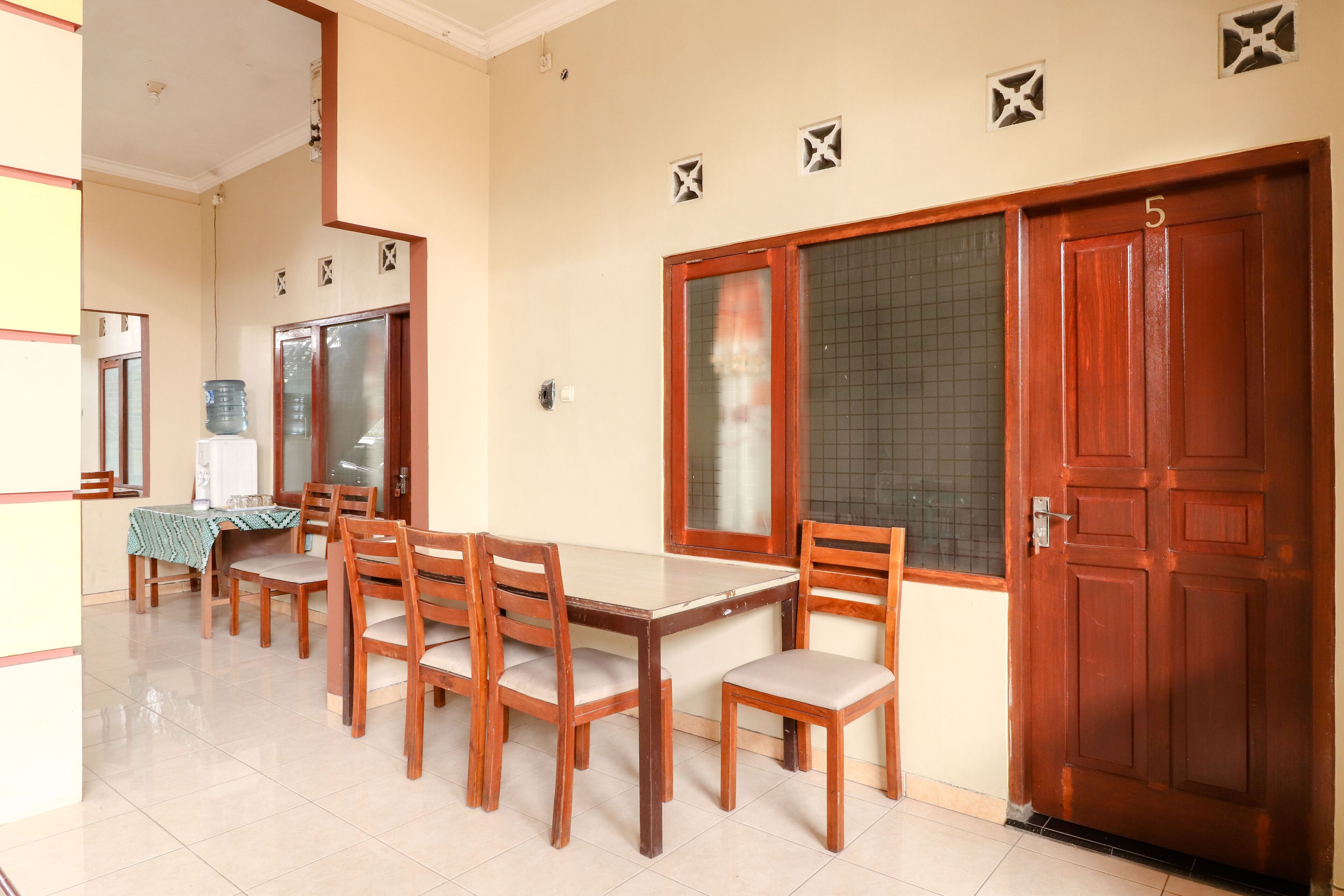 A dining area with a wooden table and chairs, a water dispenser, and a door marked with the number 5.