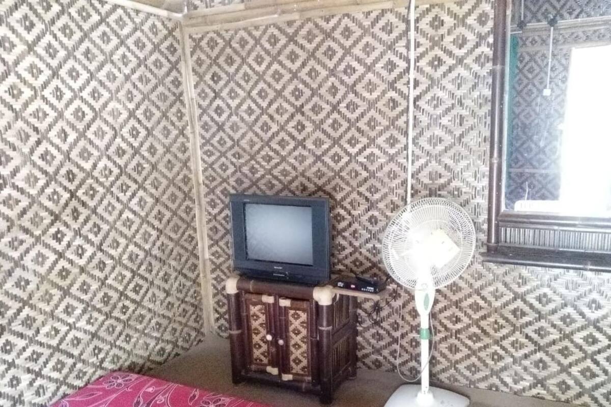 Een kamer met behang met patroon, een televisie op een houten kast, een ventilator en een raam met uitzicht.