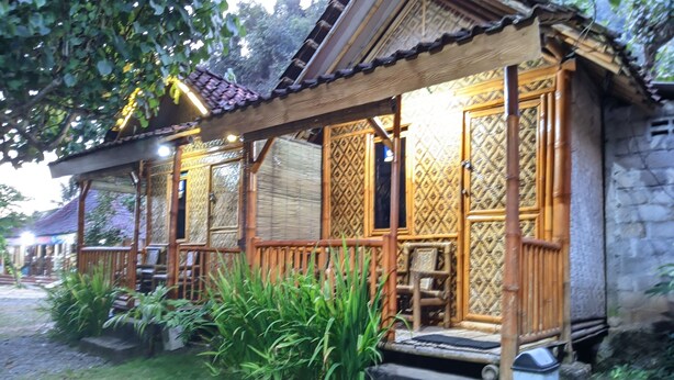 A traditional wooden house with a porch, surrounded by lush greenery. - Penginapan Griya Watukelir (Tepus)