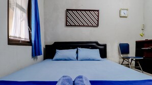 Un lit avec une couverture et des oreillers bleus, une fenêtre avec un rideau bleu, une horloge murale et une chaise.