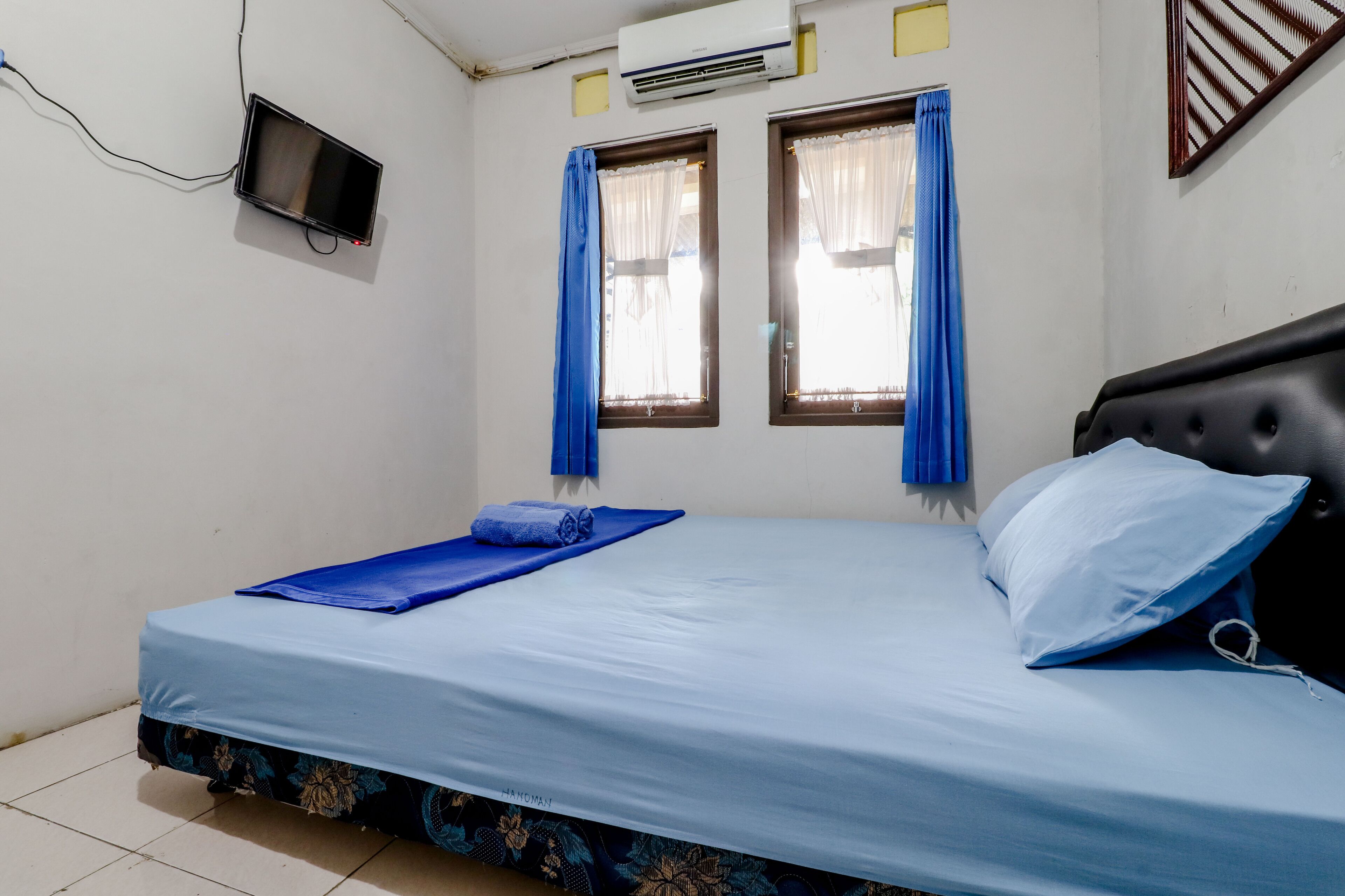 A single bed with a blue mattress and matching pillows, a small bedside table, and a wall-mounted TV.