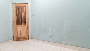 Um quarto com porta de madeira, paredes azul-claras e chão revestido de azulejos brancos.
