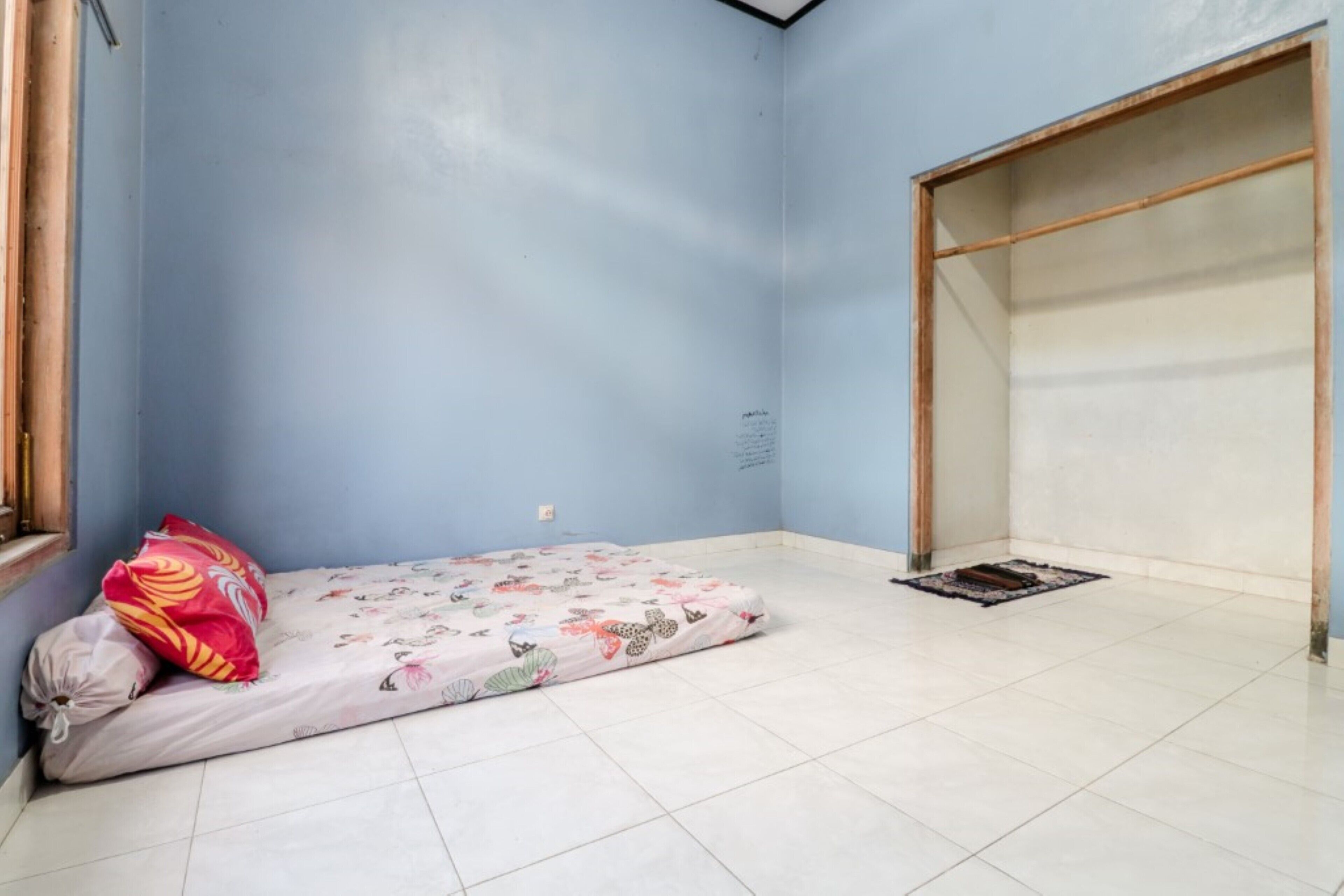 A small, sparsely furnished room with a single bed, a wooden wardrobe, and a tiled floor.