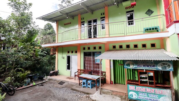 A two-story building with a green and orange facade, a balcony, and a small shop with a signboard. - Serut 2 Homestay - Hostel (Kulon Progo)