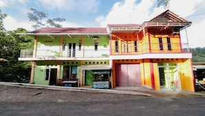 A two-story building with a green and yellow facade, a balcony on the upper floor, and a signboard in front. - Serut 2 Homestay - Hostel (Kulon Progo)