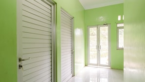 A hallway with a green wall, white doors, and a tiled floor. - Serut 2 Homestay - Hostel (Kulon Progo)