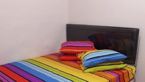 Een klein bed met een kleurrijke gestreepte dekbedovertrek en meerdere kussens in verschillende kleuren.
