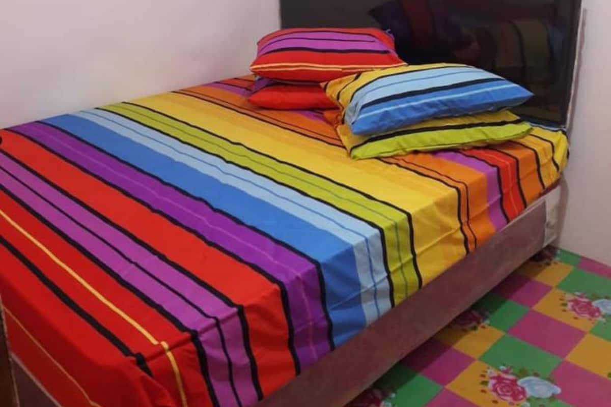 Ein kleines Bett mit einer farbenfrohen, gestreiften Tagesdecke und Kissen, ein schlichter Kopfteil und ein karierter Boden.