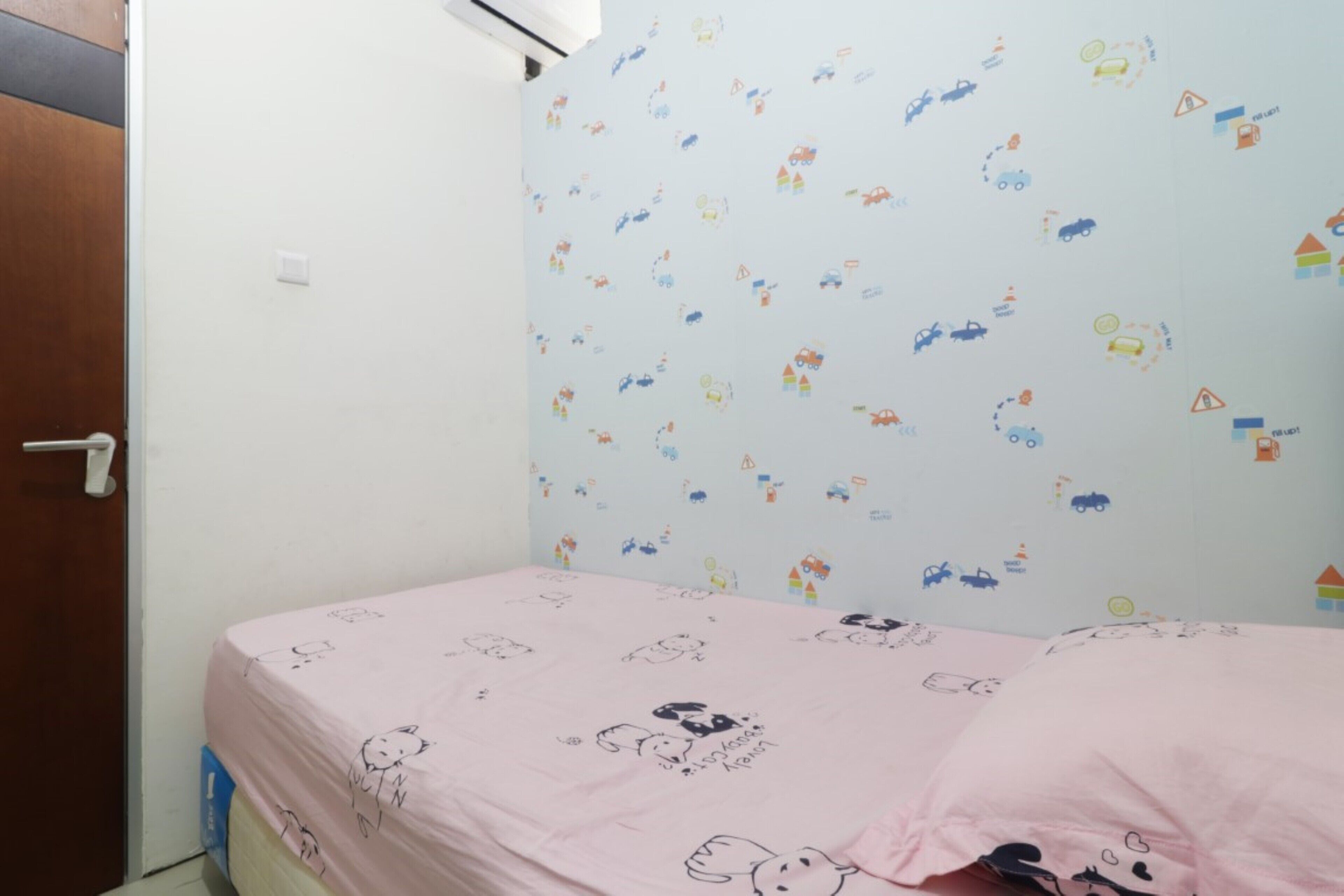 Un dormitorio con una colcha rosa adornada con personajes de dibujos animados, una pared blanca decorada con pegatinas de colores y una puerta de madera.