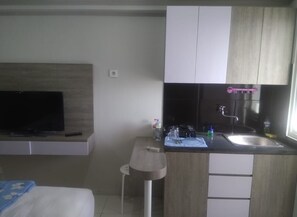 A compact hotel room with a bed, a TV, a small kitchenette with a sink, and a window. - Apartment Gunawangsa Merr by Rava (Surabaya)