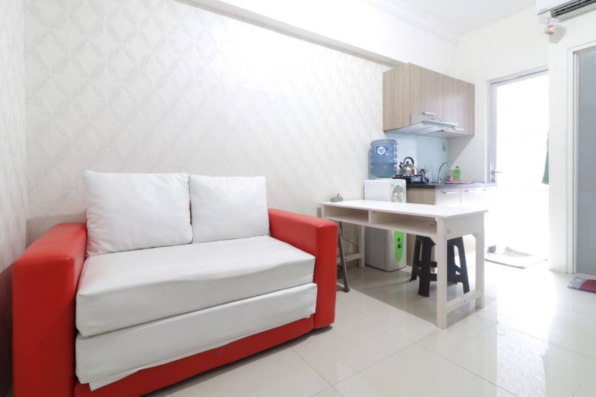 A modern living room with a red and white sofa, a white table, and a kitchenette area.
