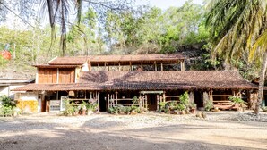 A rustic two-story building with a tiled roof and wooden structure, surrounded by potted plants and trees. - Penginapan Joko Samudro (Wonosari)
