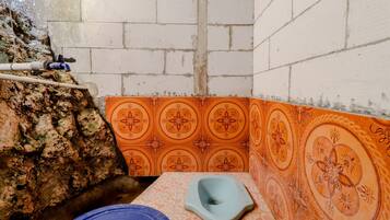 A small bathroom with a toilet, a blue basin, and a water pipe.