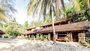 A traditional wooden building with a tiled roof, surrounded by palm trees and greenery. - Penginapan Joko Samudro (Wonosari)