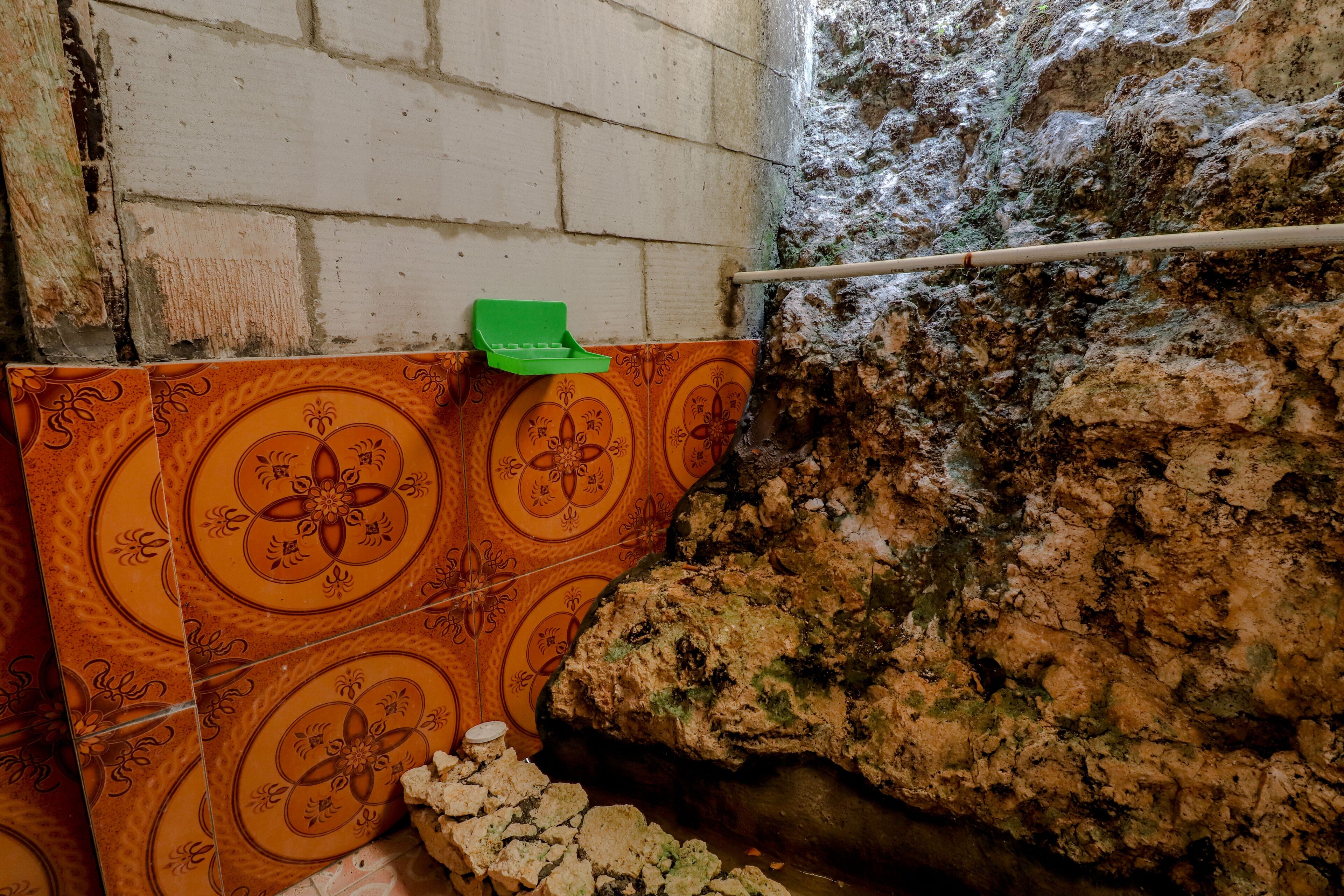 A bathroom with tiled walls, a green cleaning brush, and a stone wall.