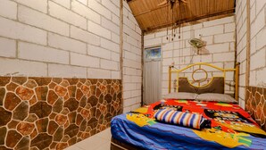A small, narrow room with a bed, a fan, and a door. - Penginapan Joko Samudro (Wonosari)