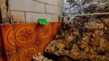Un baño con baldosas estampadas, un cepillo de limpieza verde y una pared rocosa.