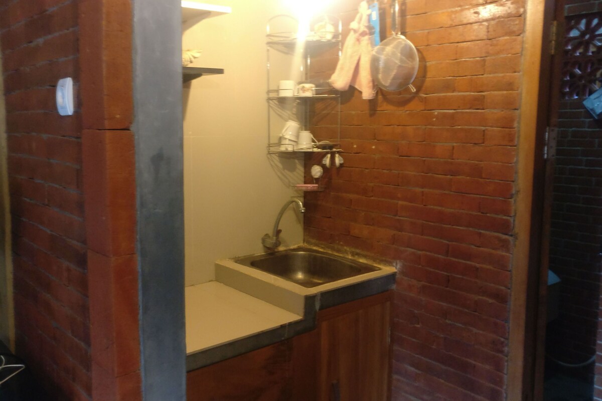 A compact kitchen with a sink, a small countertop, and a brick wall.