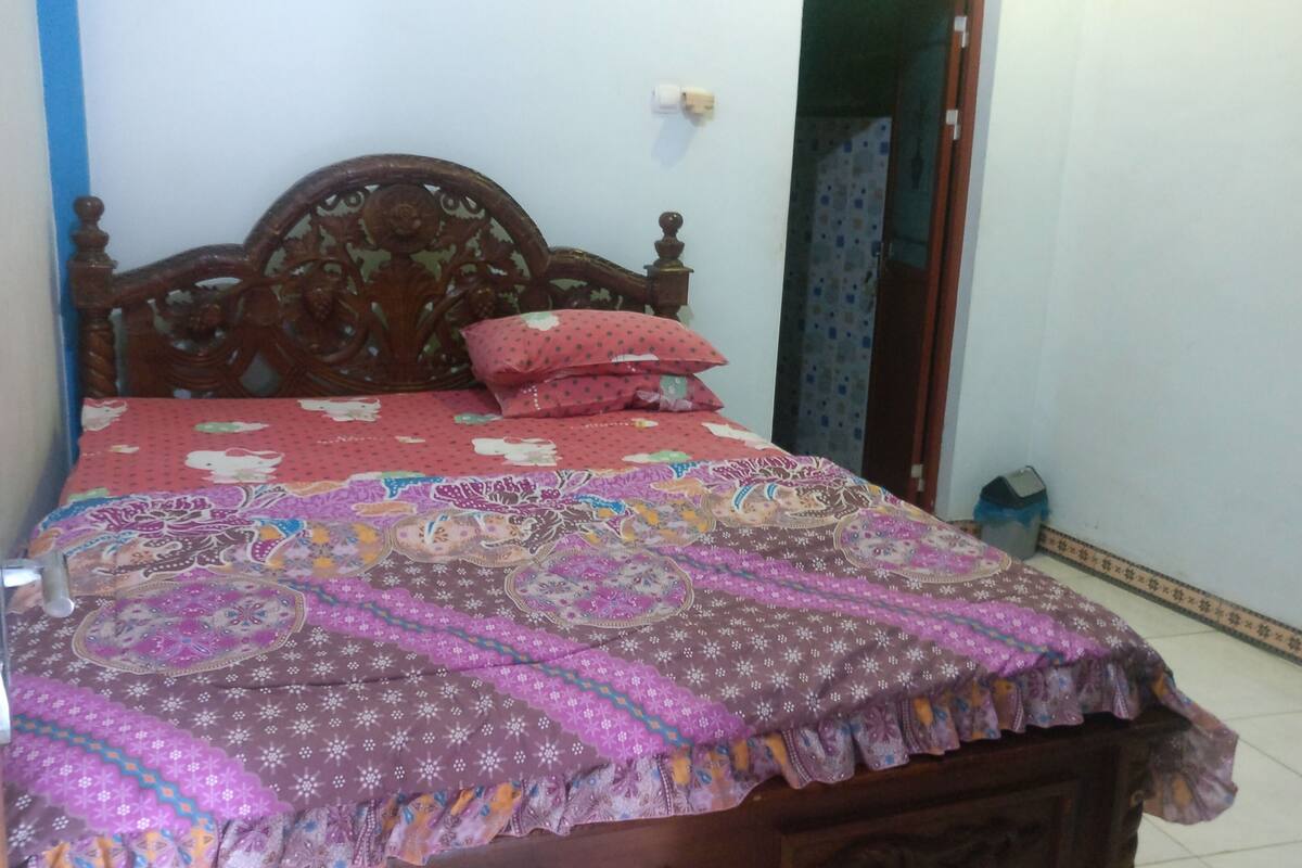 Un dormitorio con cama de madera, colcha estampada y almohada roja.