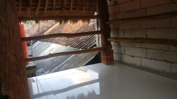 A room with a thatched roof visible through a wooden frame, a tiled floor, and a brick wall. - Jogo Segoro Homestay (Wonosari)