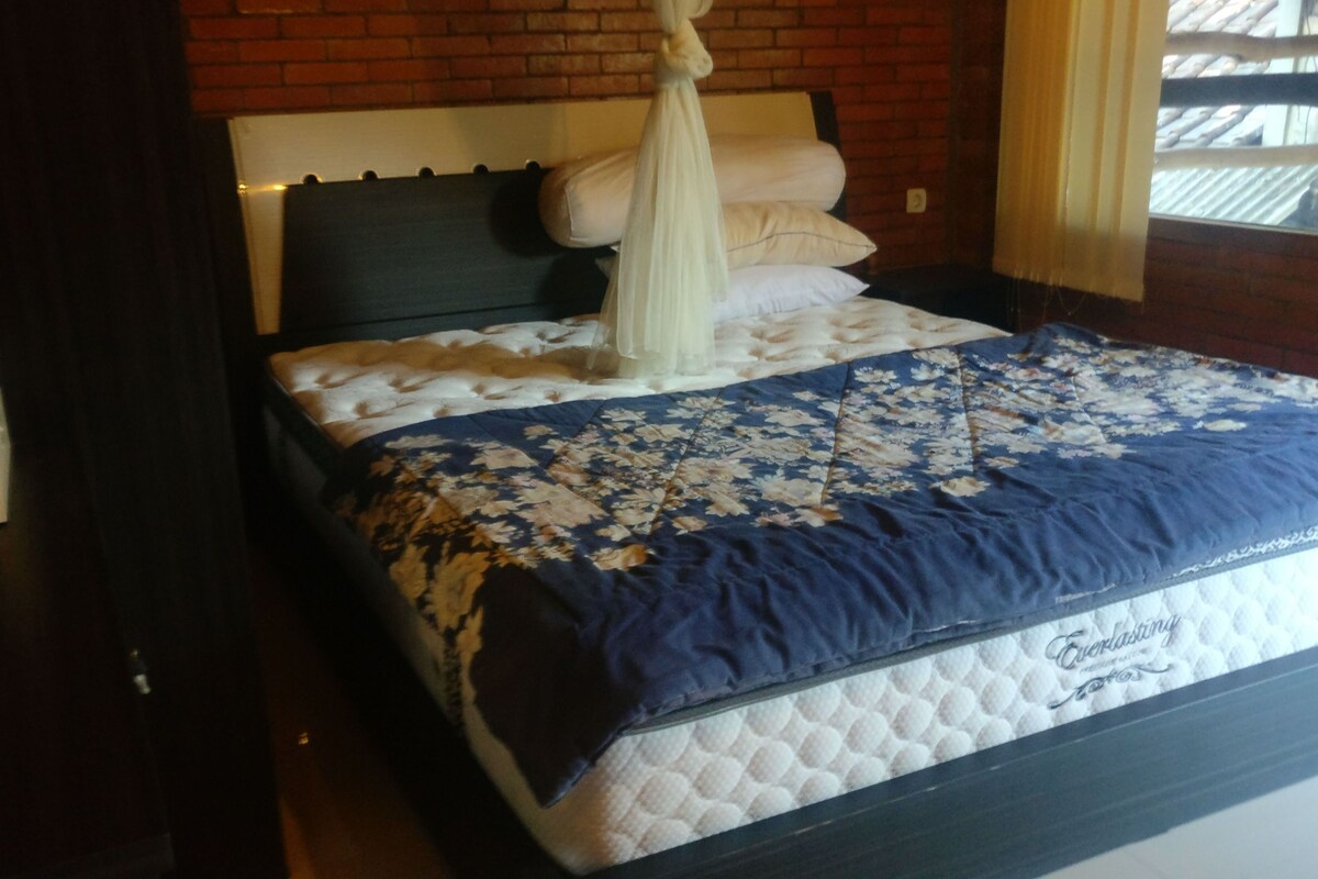A bed with a canopy, a floral bedspread, and a quilted mattress.