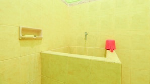 Un baño con azulejos amarillos, una ducha, un jabonera y una toalla roja.