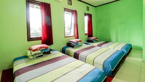 Una habitación con tres camas, cada una con colcha a rayas y almohadas, y cortinas rojas en las ventanas.