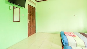 Una habitación con cama, televisor montado en la pared, puerta de madera y suelo de baldosas.