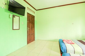 A room with a bed, a television mounted on the wall, a wooden door, and a tiled floor. - Penginapan Roro Mendut Syariah by Zuzu (Mungkid)