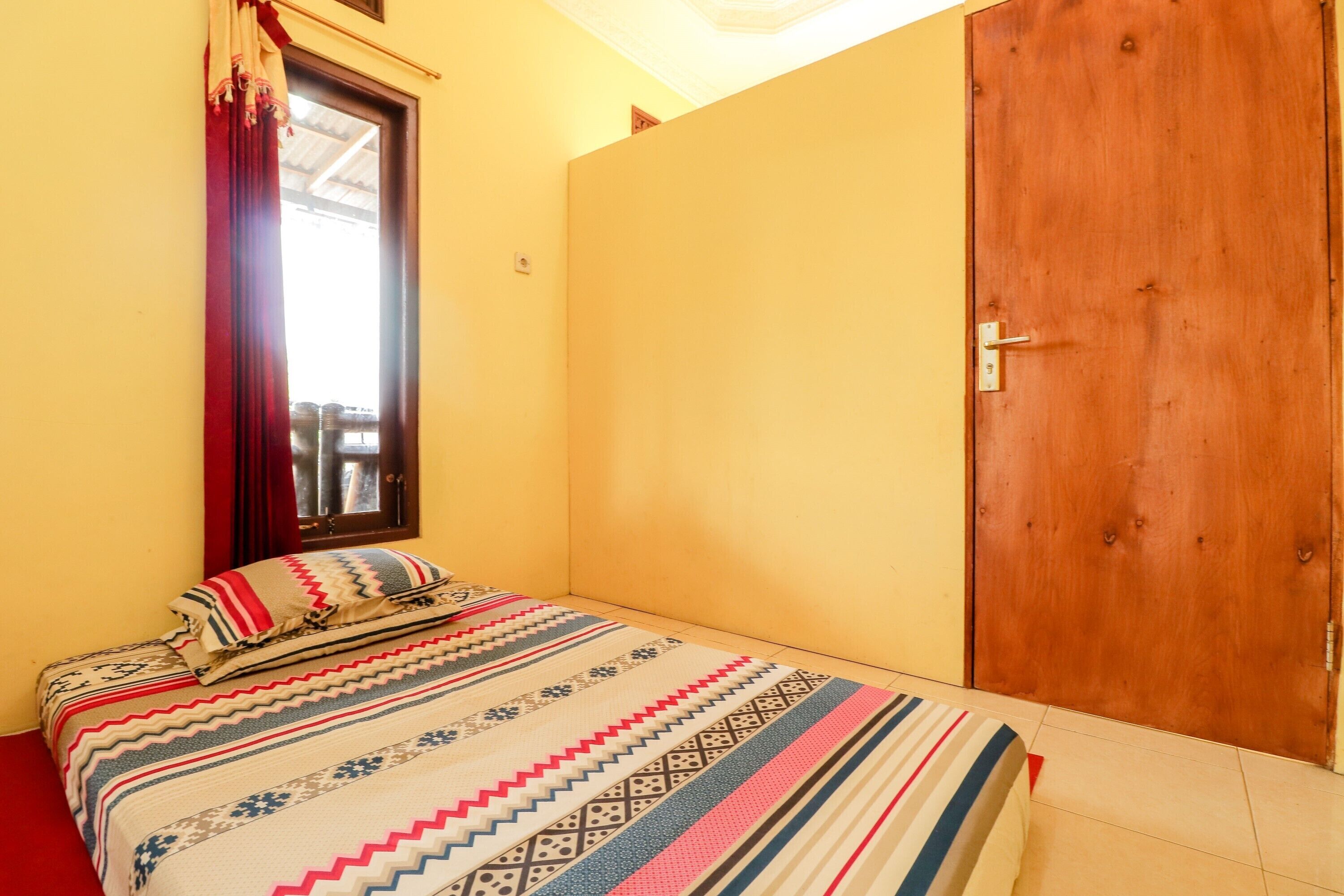 A small, single-bed room with a wooden door and a window with curtains.