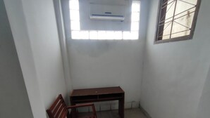 A small room with a wooden bench, a wooden chair, a window with bars, and an air conditioning unit. - Charisma Residence Syariah (Surabaya)