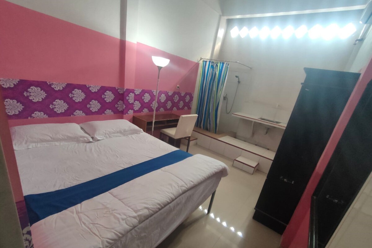 A hotel room with a bed, a desk, a chair, a wardrobe, and a shower area.
