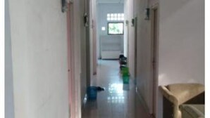 A narrow hallway with a tiled floor, a door at the end, and a window with blinds. - Charisma Residence Syariah (Surabaya)