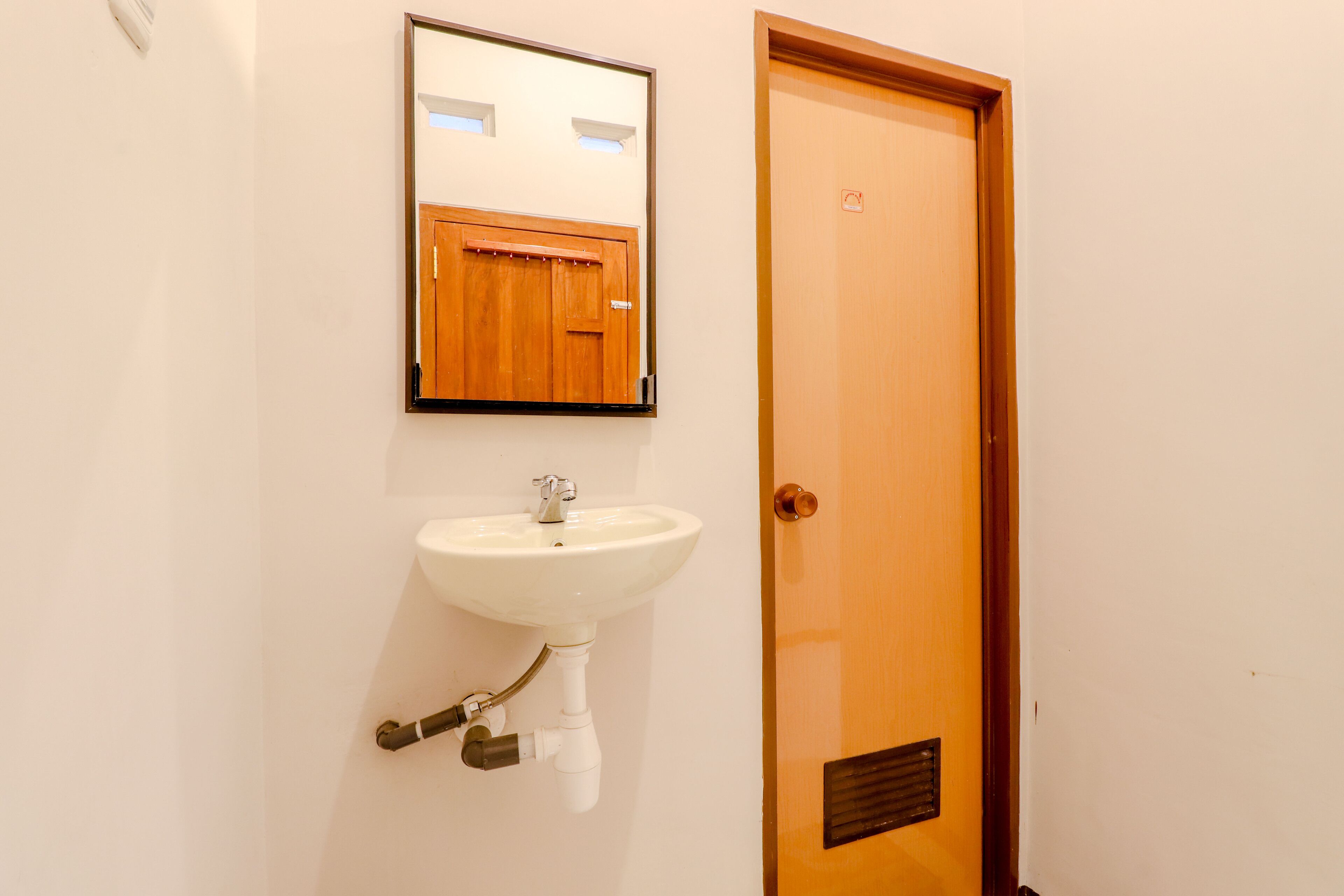A bathroom with a white sink, wooden door, and a mirror above the sink.