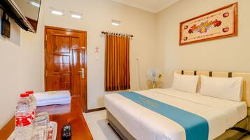 A hotel room with a bed, a table with a remote control, water bottles, and a tray.