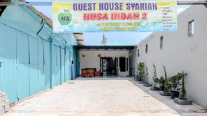 A guest house with a paved entrance, a blue building on the left, and potted plants along the right wall.
