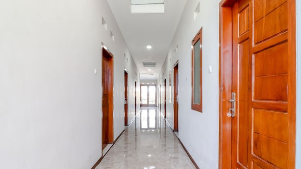 A long, narrow hallway with wooden doors on both sides and a shiny tiled floor.