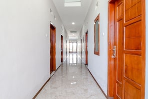 Un pasillo largo y estrecho con puertas de madera a ambos lados y un suelo de baldosas brillantes.