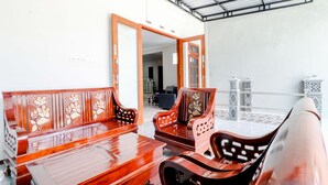 A traditional wooden sofa set with intricate carvings, a matching wooden table, and a clear view of the adjacent room through an open doorway.