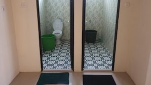 Un baño pequeño y cerrado con un inodoro, un cubo verde y un bote de basura negro.