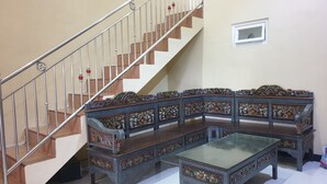 Una escalera con barandilla de metal y escalones de madera, un banco de madera tallada tradicional y una mesa de centro con superficie de vidrio.